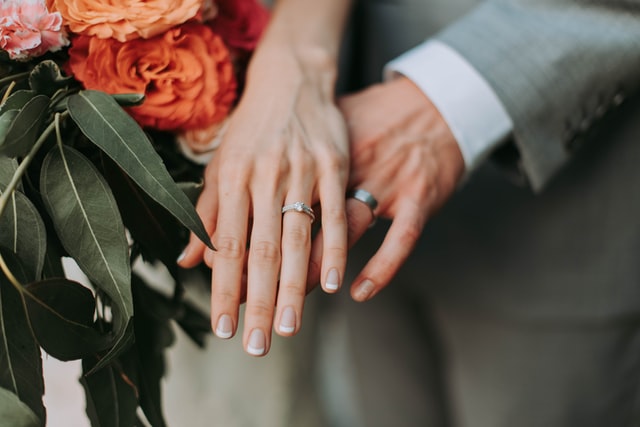 Händer på ett bröllopspar, som visar deras förlovningsringar.